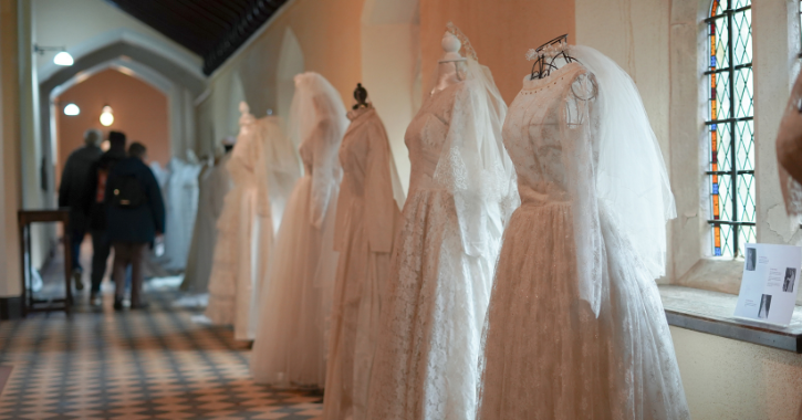 People walking past wedding dresses on display inside Ushaw Historic House.
